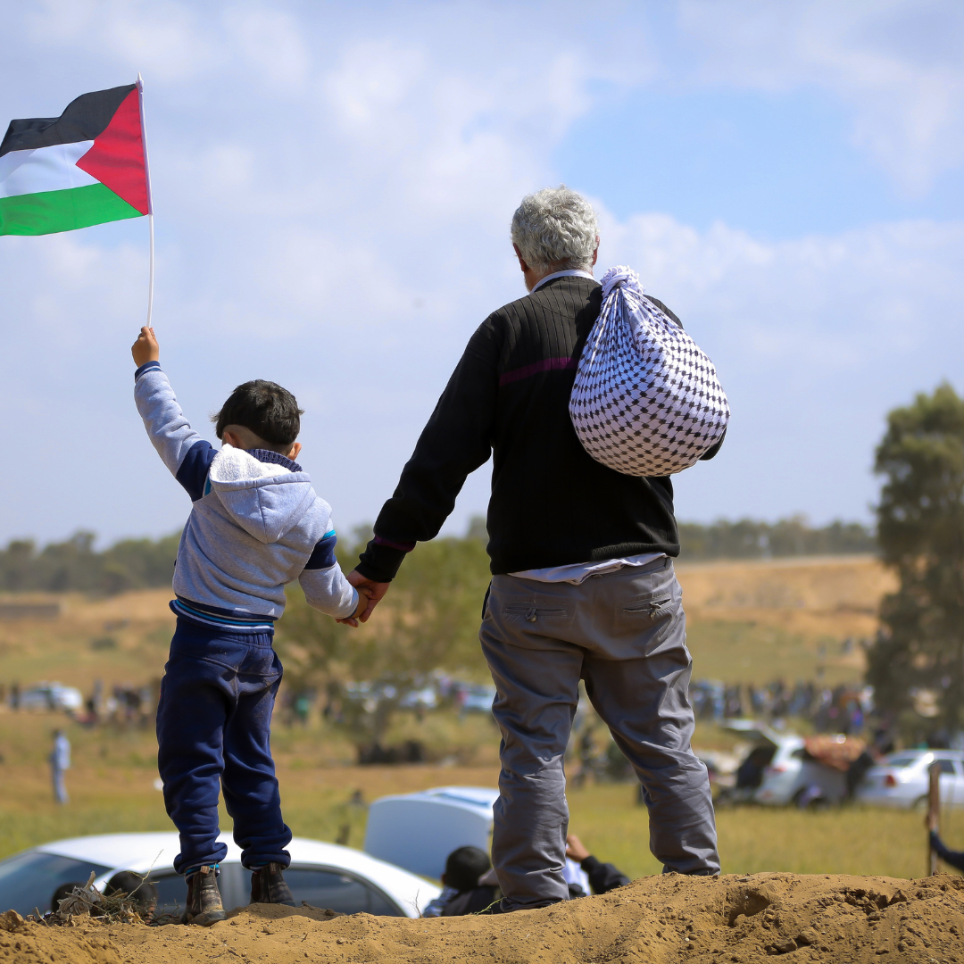 Young boy holding hands with an older man as her waves a Palestinian flag. Photo From Pixabay.
